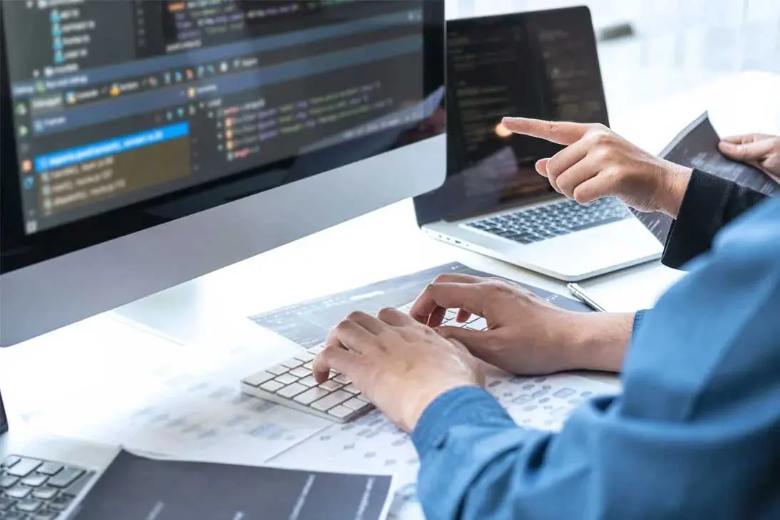 Dos desarrolladores analizando código en un monitor y un portátil, representando el proceso técnico de la integracion ERP EDI