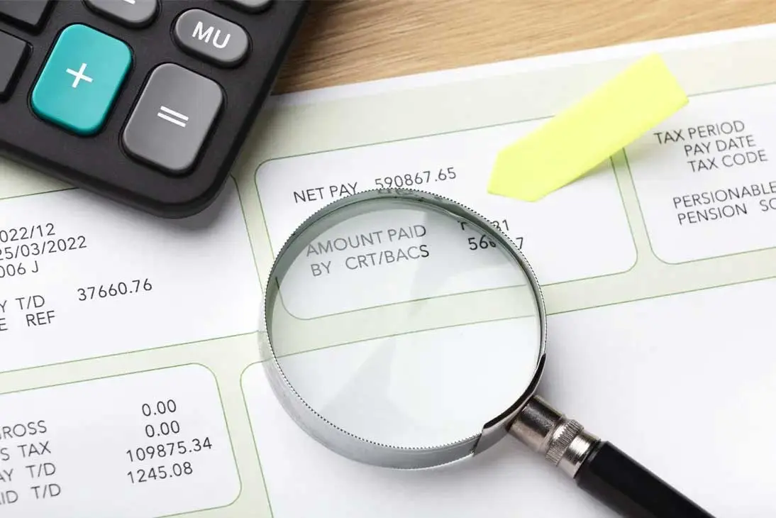 Primer plano de una calculadora, nóminas y una lupa que amplía datos financieros para el análisis contra el fraude fiscal